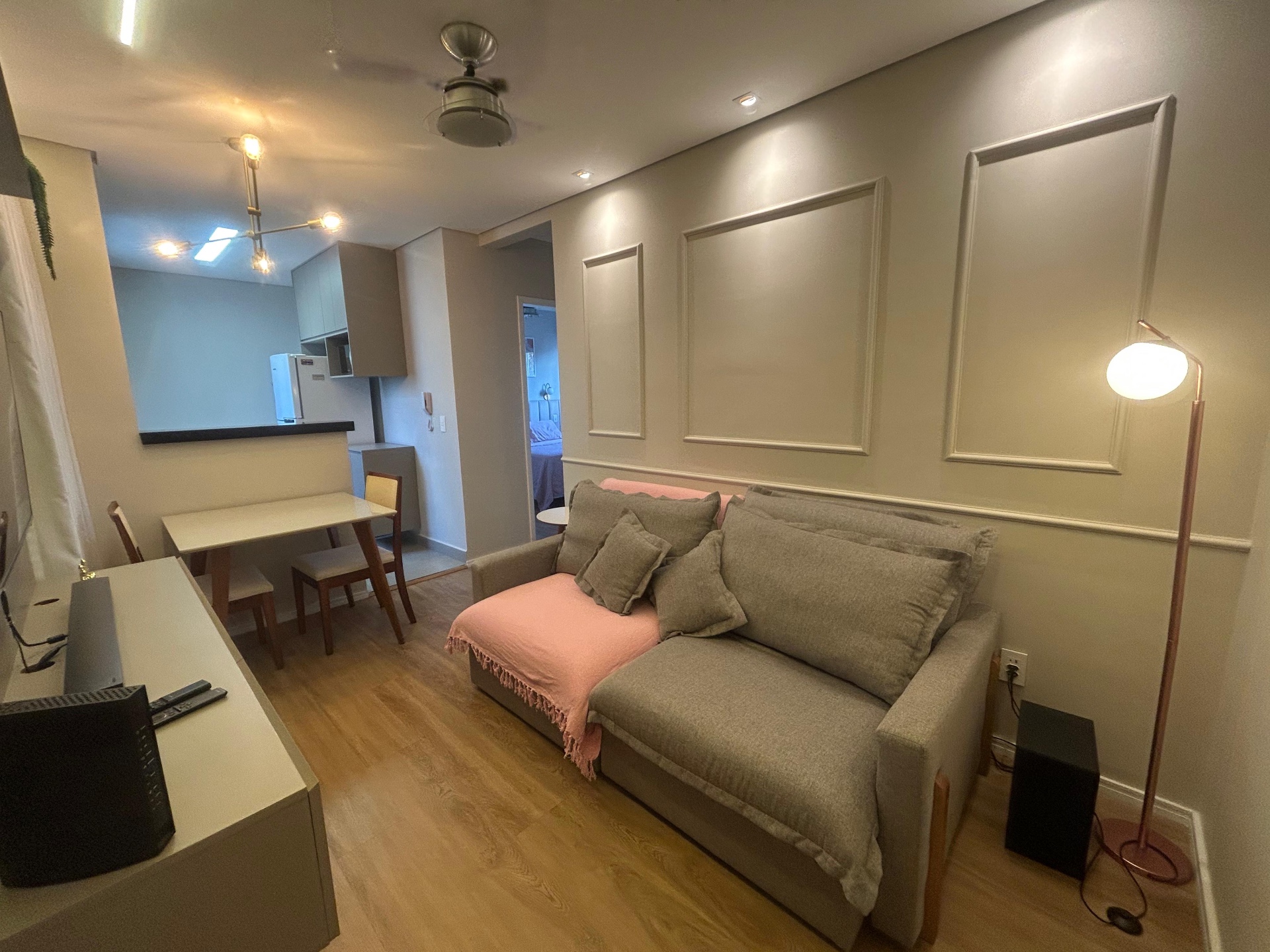 Sala integrada com sofá, mesa de jantar e cozinha americana ao fundo