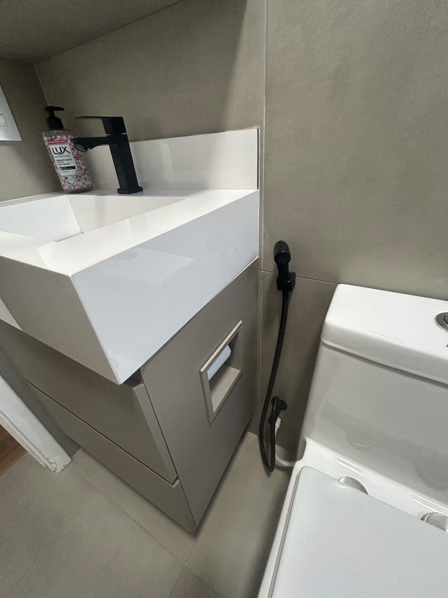 Detalhe da bancada branca do banheiro com torneira preta e ducha higiênica